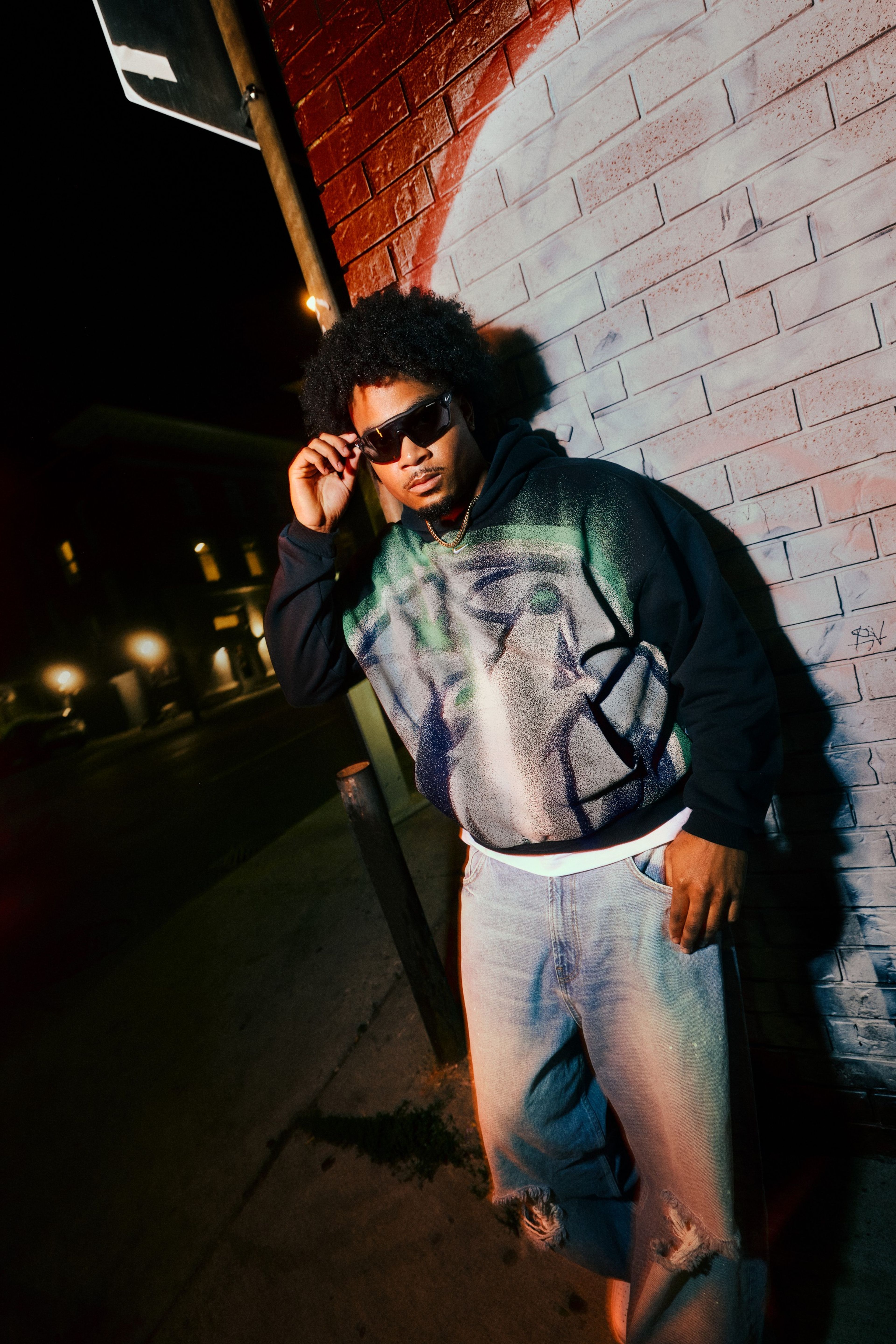 A man wearing sunglasses poses for a photo in front of a brick wall while wearing a Minnesota Timberwolves hoodie from Nike’s NBA Standard Issue Collection.