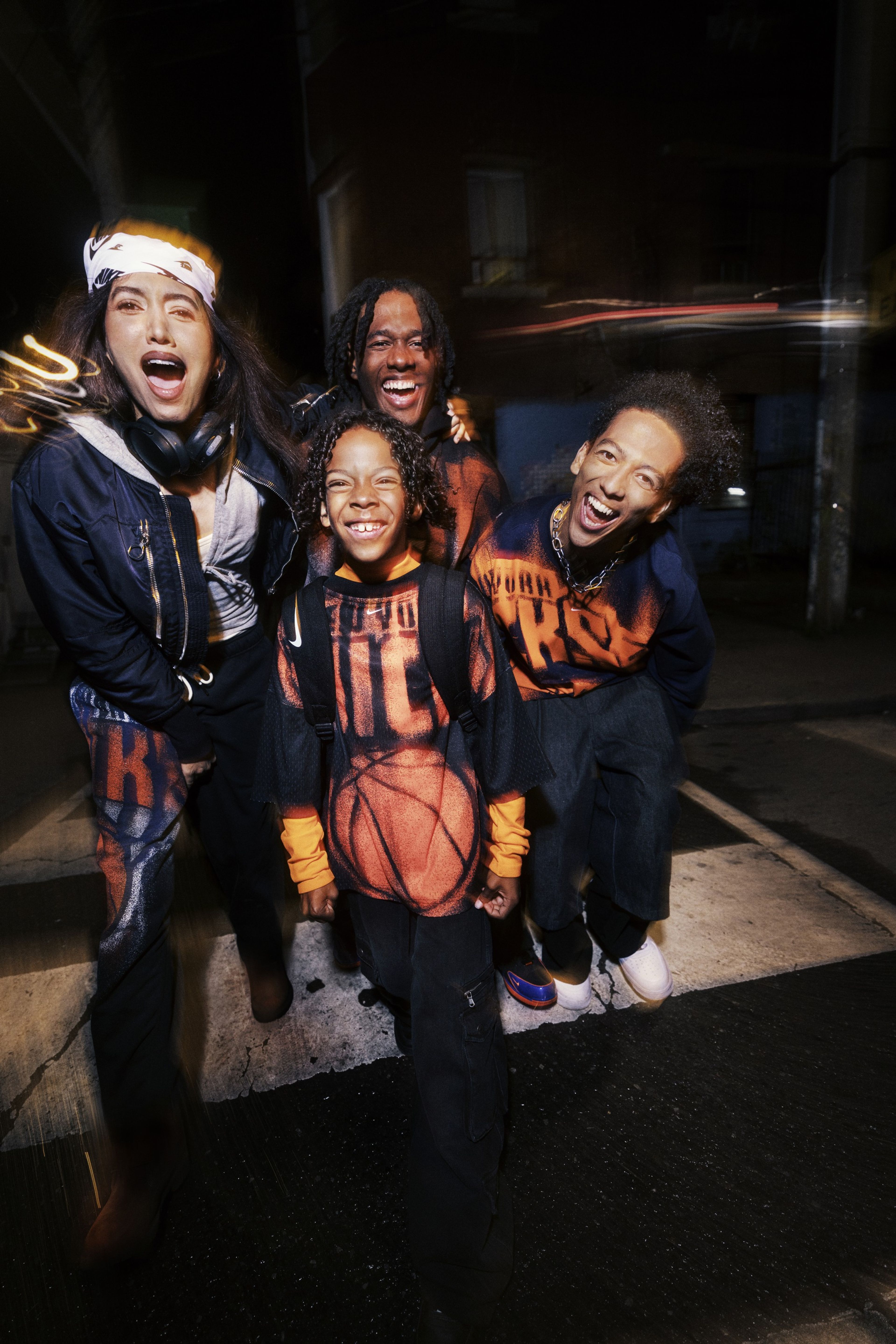 Four people wear New York Knicks apparel from Nike’s NBA Standard Issue Collection, posing for the camera against a blurry background.