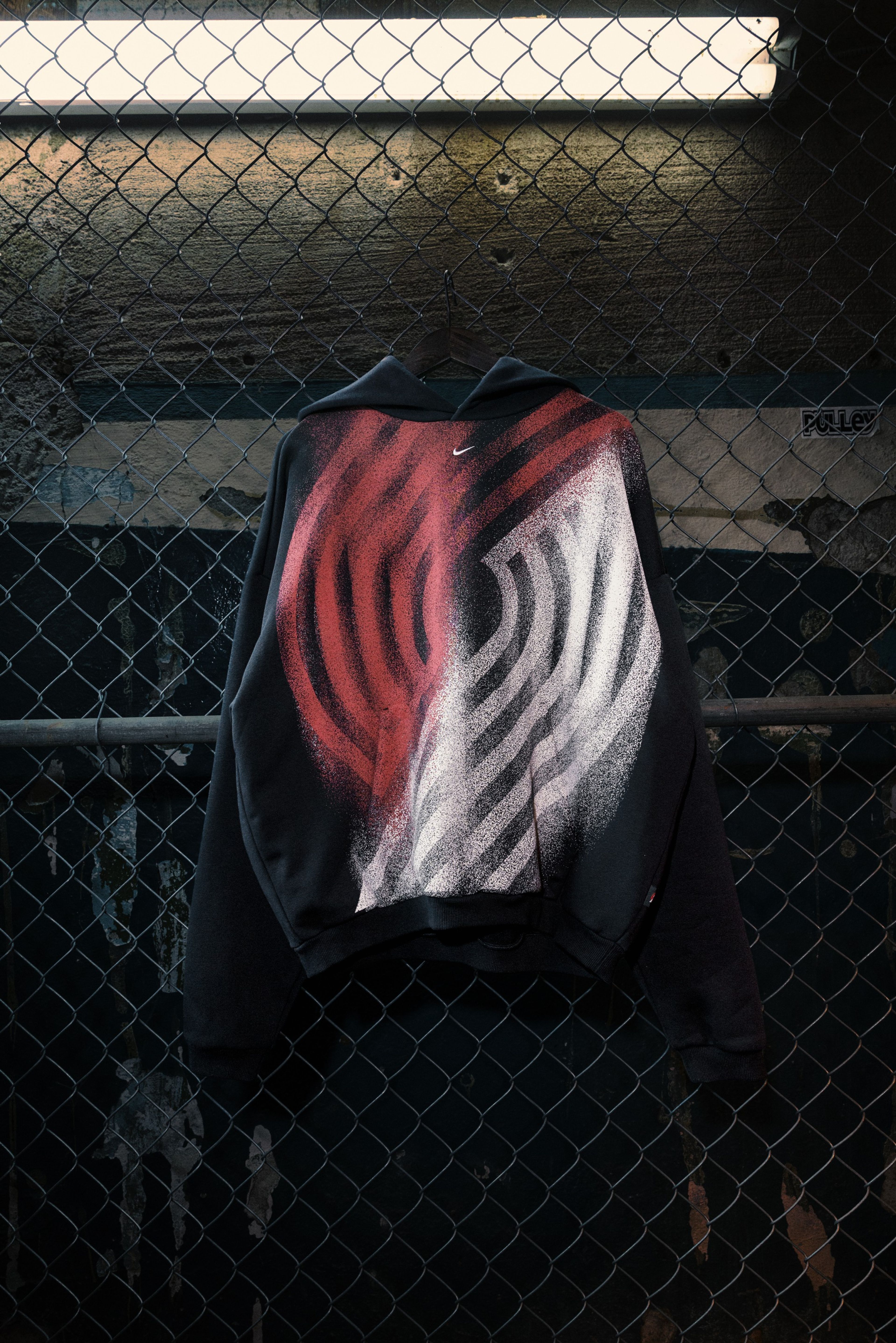 A black hoodie with a large Portland Trail Blazers logo is pictured against a chain-link fence.