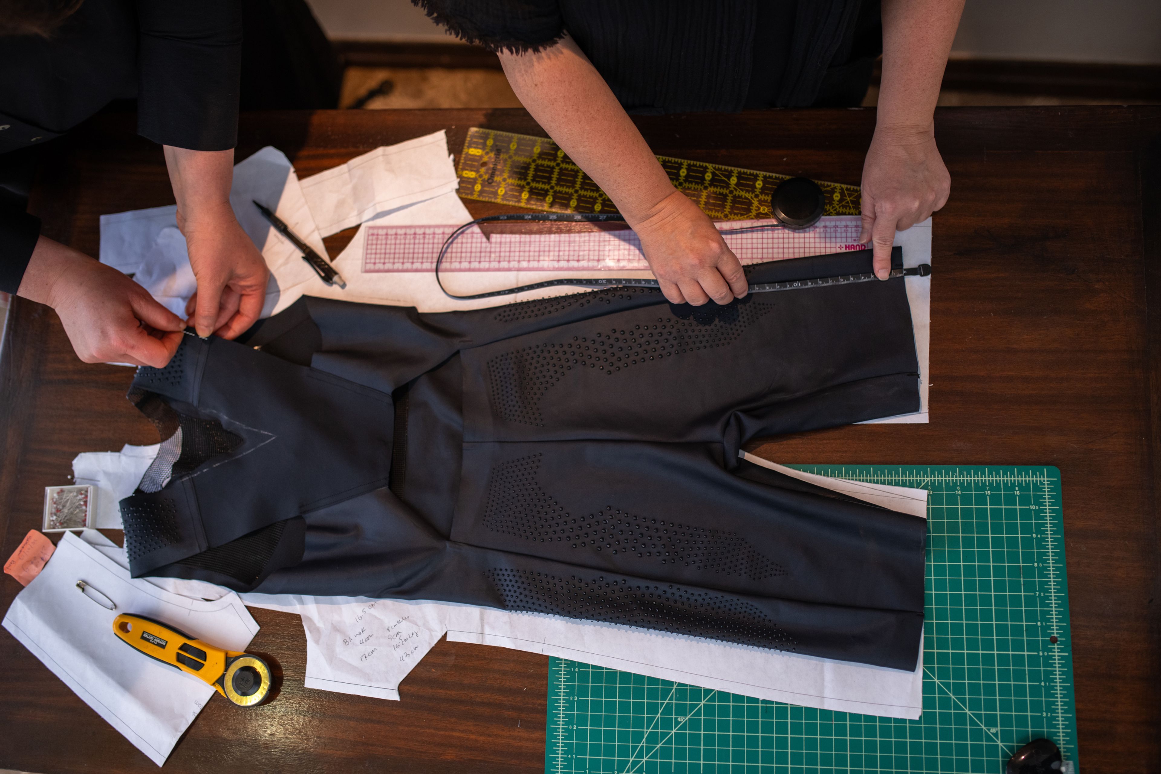 Two people work on a body suit design that's sitting flat alongside other materials and tools on a table.
