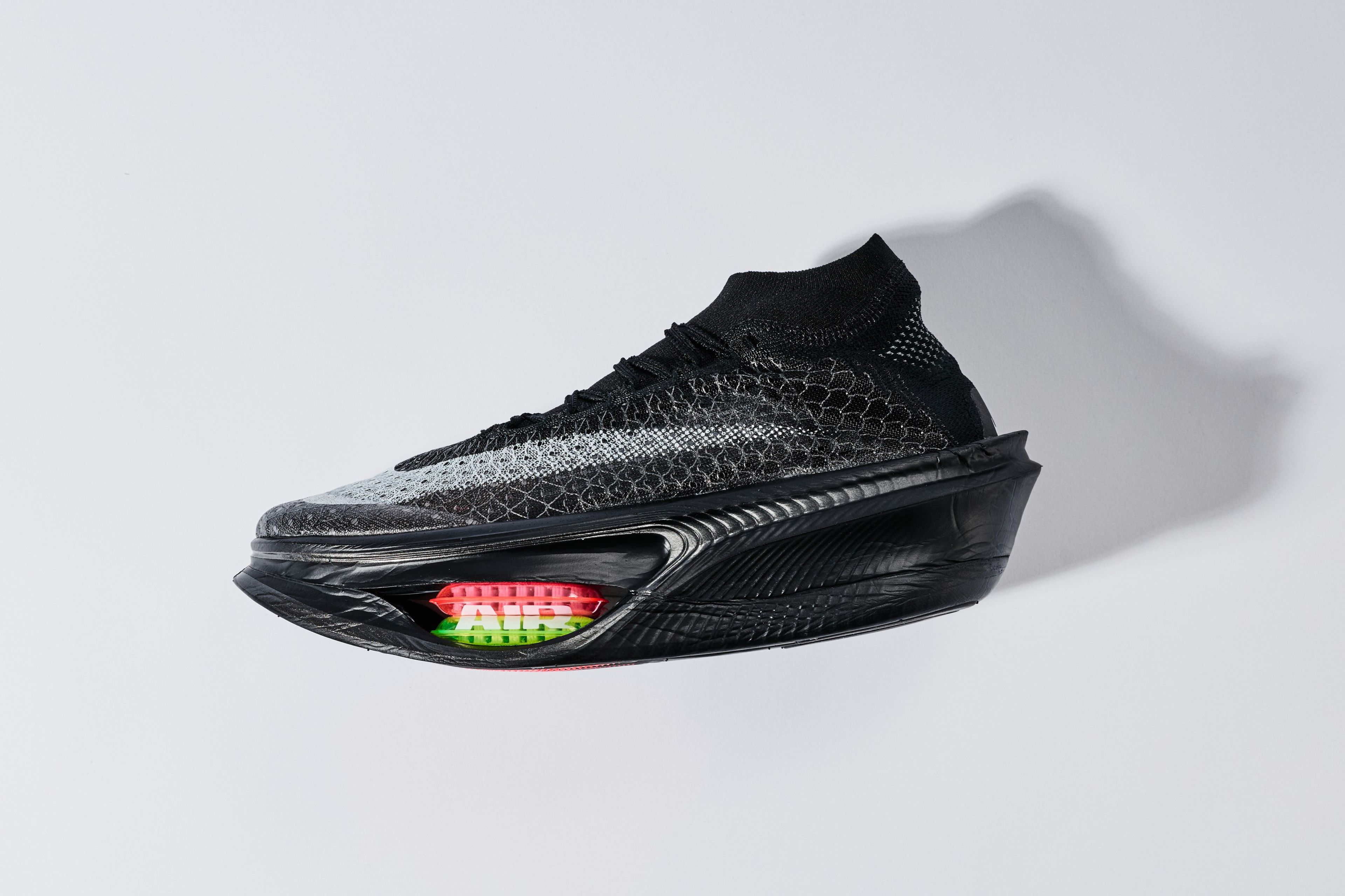 A black Nike Apex running shoe with a visible red and green Air cushioning unit in the sole, featuring a textured knit upper and sock-like collar.